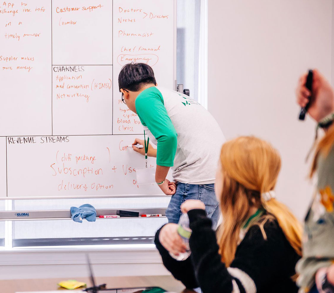 man writing on dry erase board in front of room