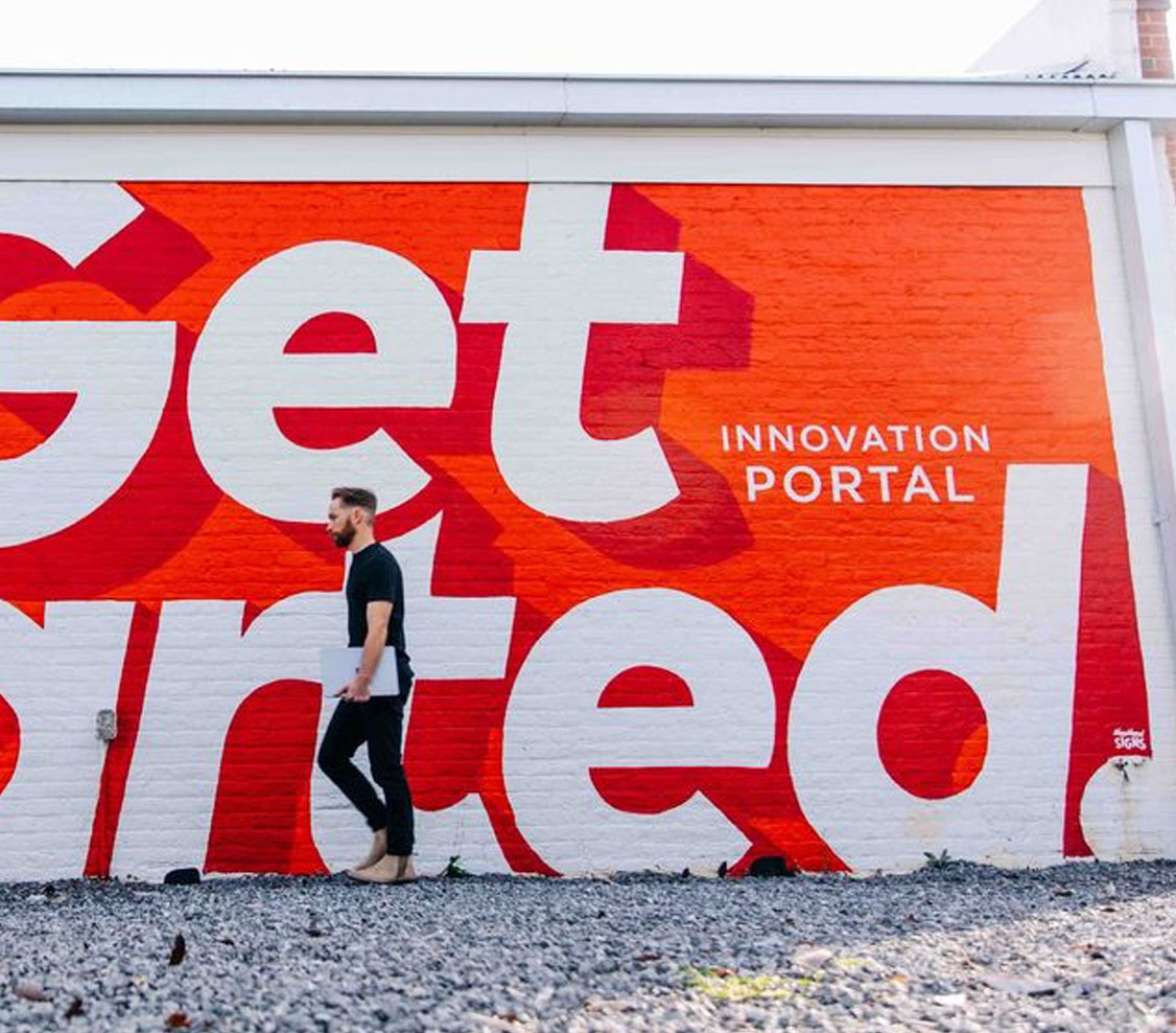 get involved innovation portal mural that says "get started" large on wall with young man walking in front of letters